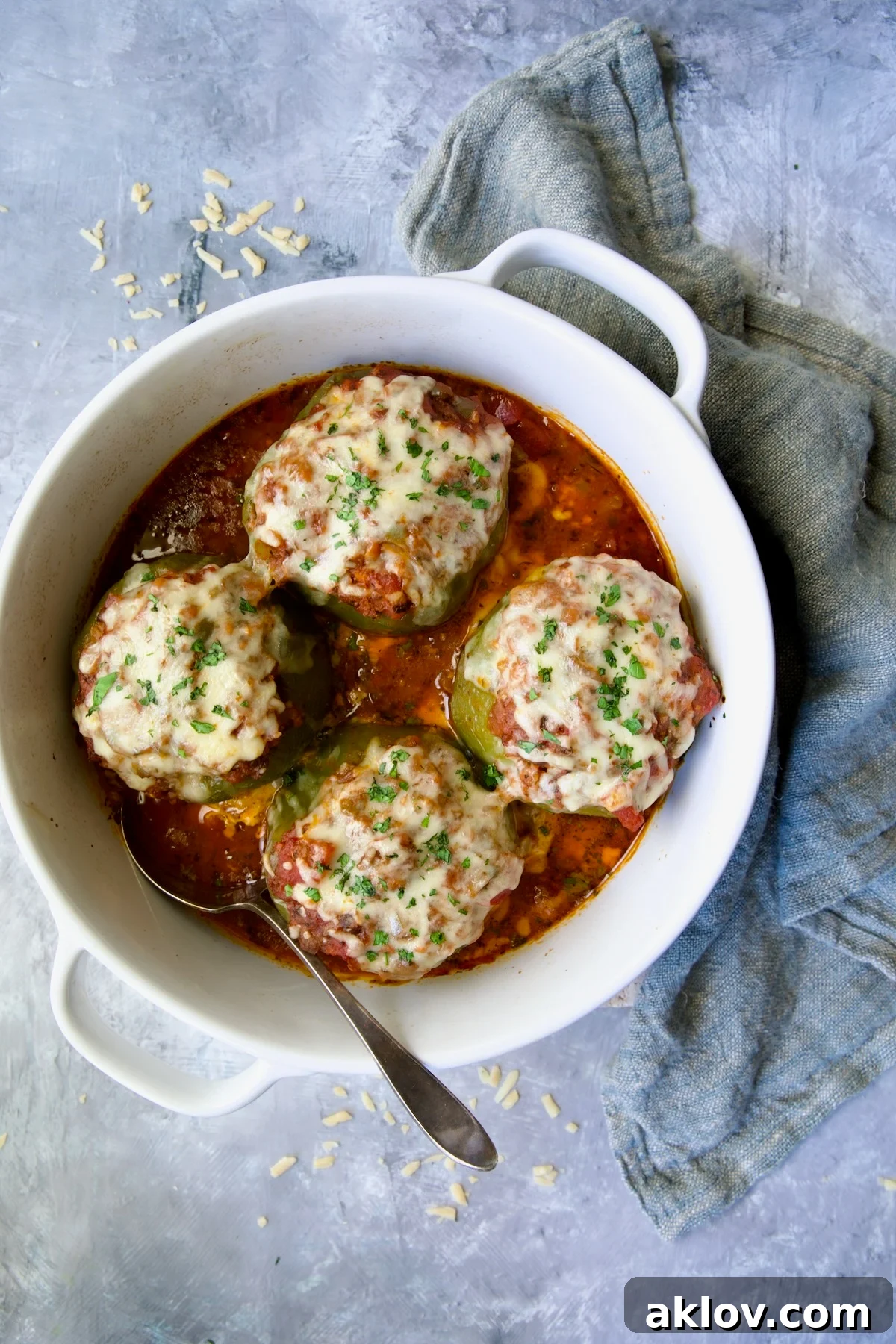Four Italian Stuffed Peppers in deep white round baking dish with a serving spoon and blue napkin, ready to be enjoyed.