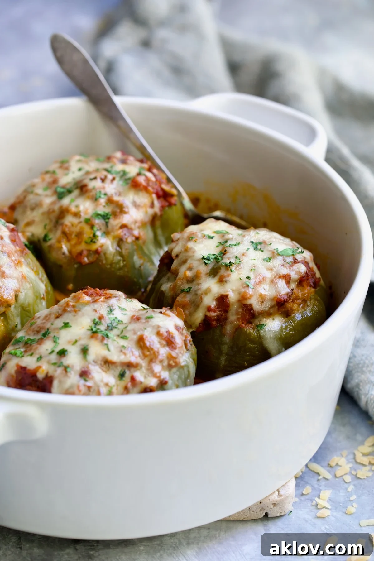Four Italian Stuffed Peppers in deep white round baking dish with a serving spoon, highlighting the cheesy topping.
