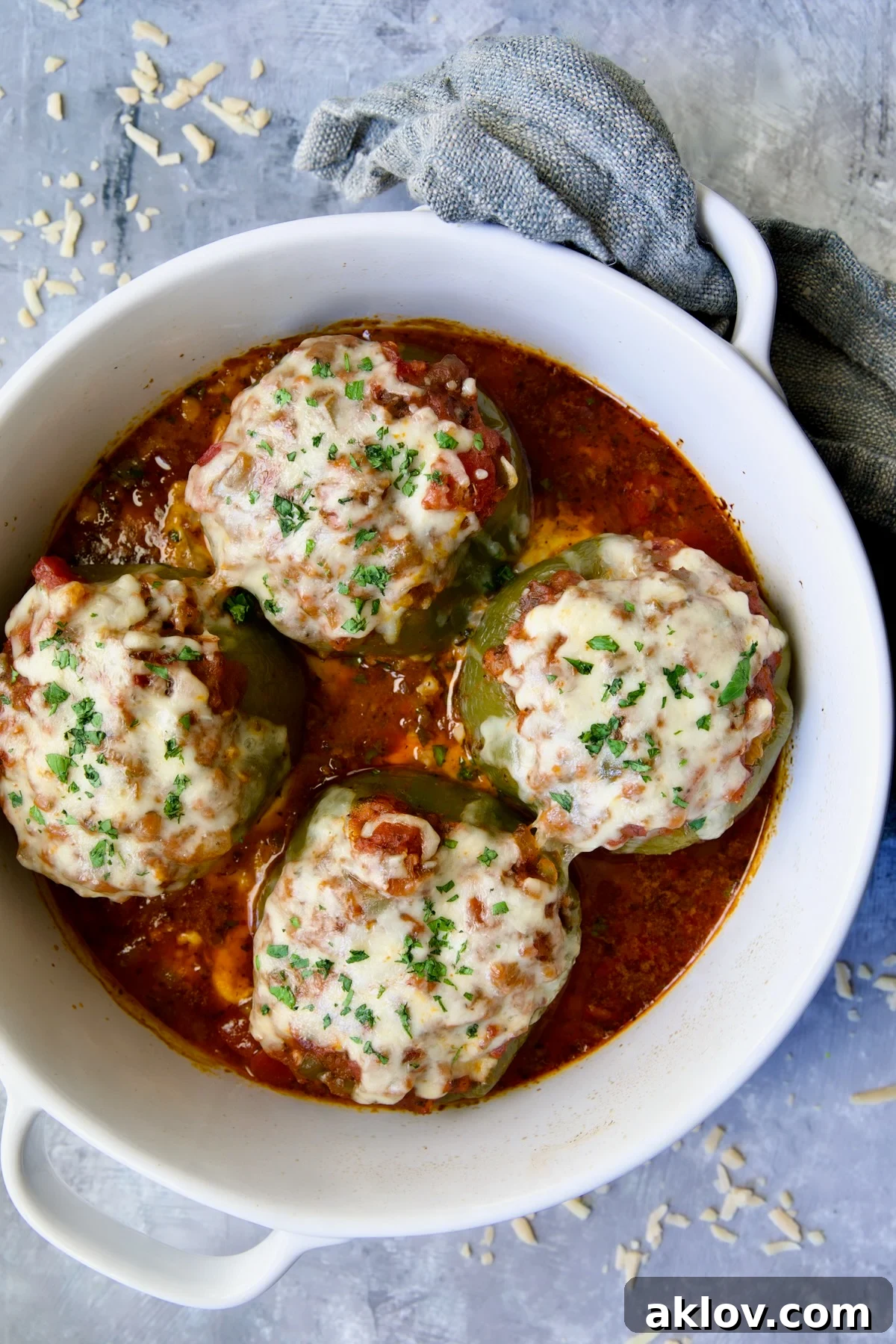 Four Italian Stuffed Peppers in deep white round baking dish, ready to be served, with a rustic kitchen towel.