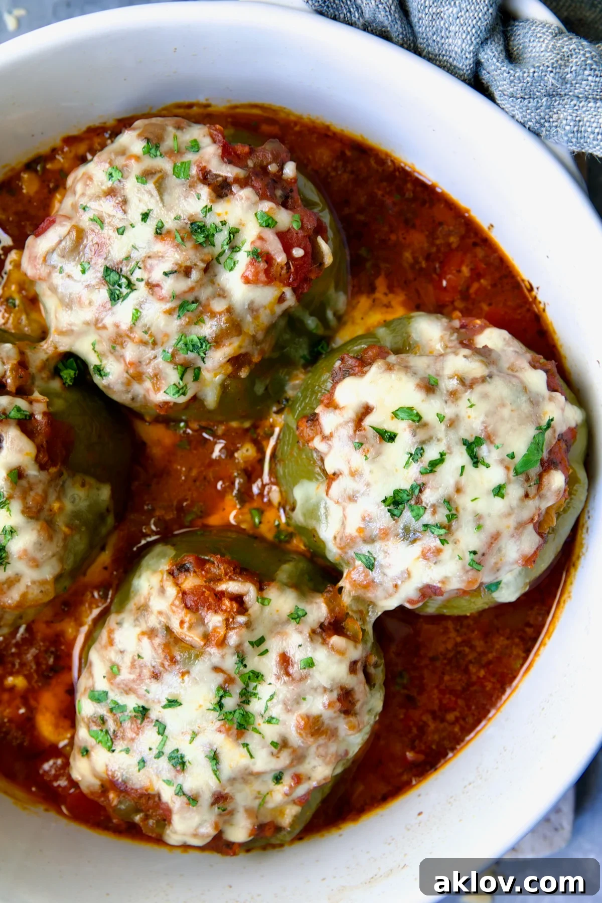 Three Italian Stuffed Peppers in deep white round baking dish, garnished with fresh parsley.