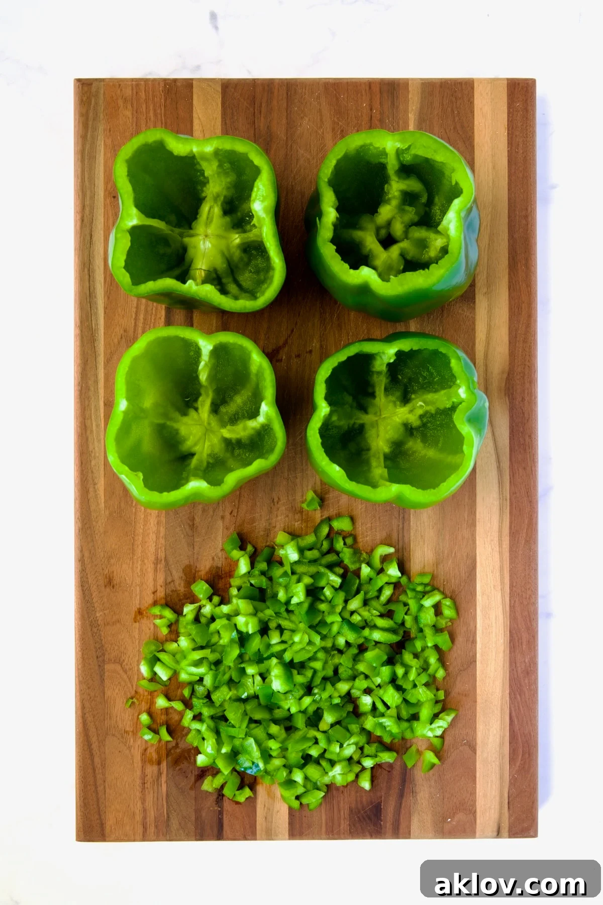 Chopped green bell pepper tops on a wooden cutting board next to hollowed out peppers.