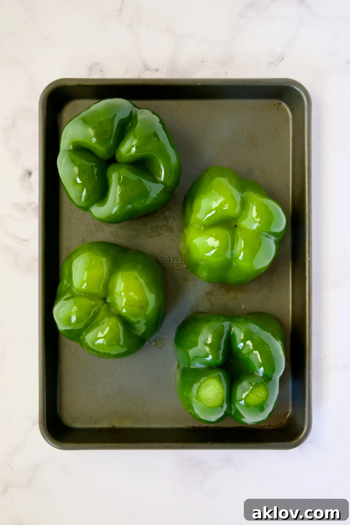 Four green bell peppers turned upside down on a rimmed sheet pan before baking.