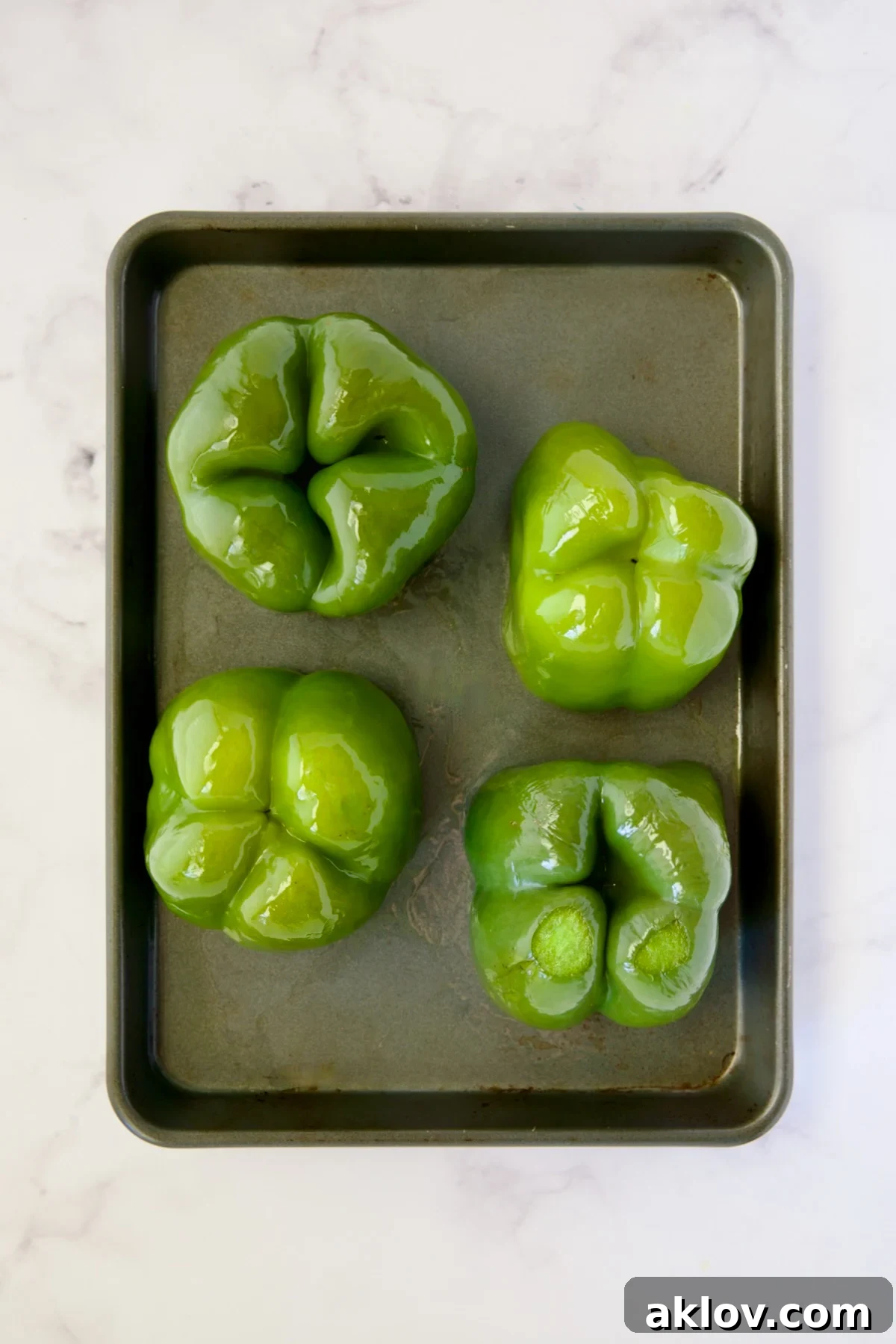 Four green bell peppers turned upside down after being roasted for 15 minutes, with released liquid visible.