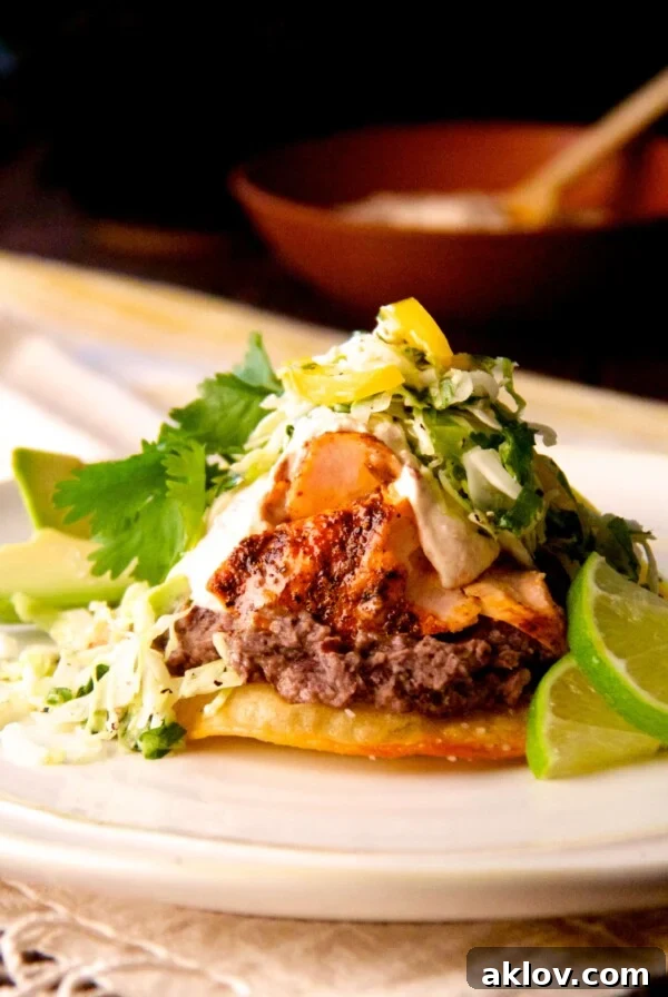 Salmon and Black Bean Tostadas with Cilantro - Lime Slaw and Chipotle Crema on white plate with lime wedges.