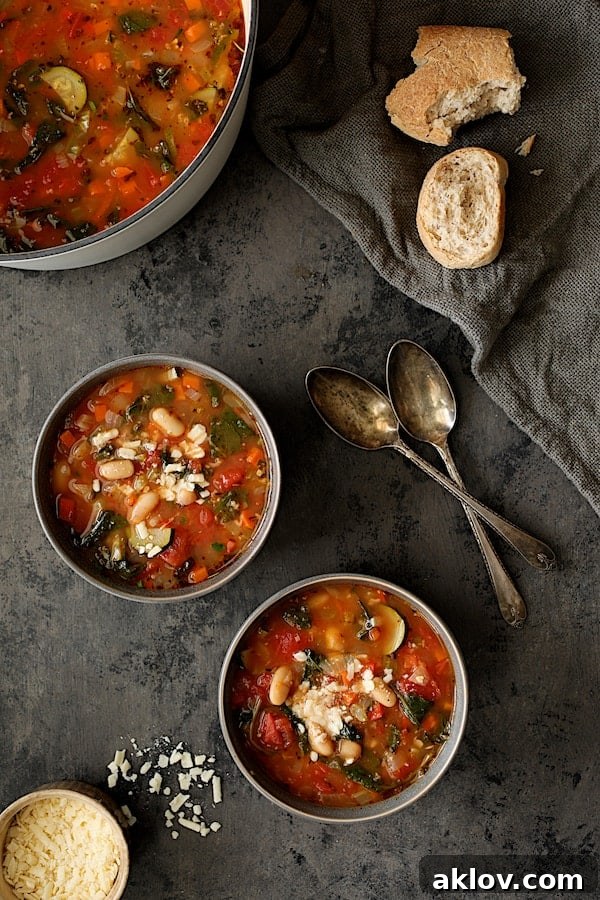 Photo of two servings of Smoky Spanish Vegetable and White Bean Soup with Kale with cheese and broken bread.