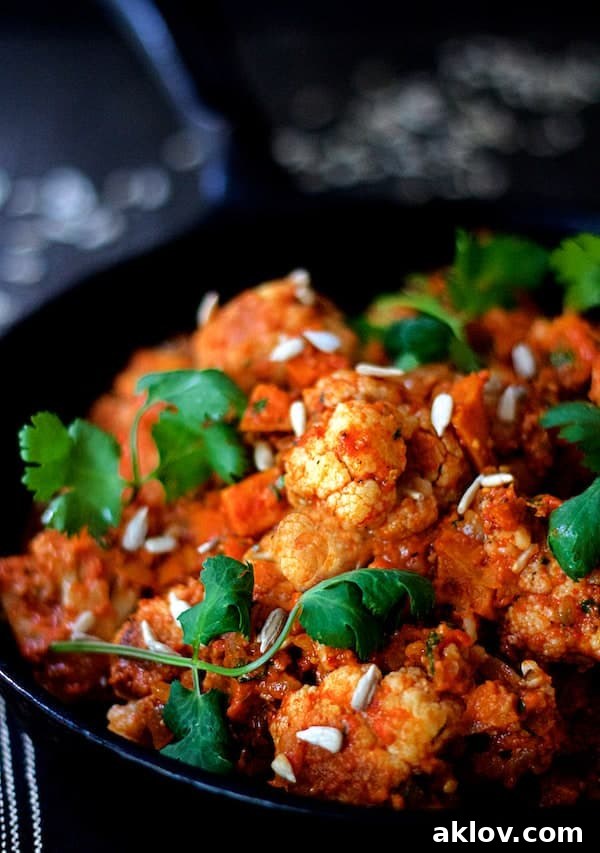 Photo of Cauliflower and Sweet Potatoes in Roasted Red Pepper Mole in cast iron skillet garnished with cilantro and sunflower seeds.