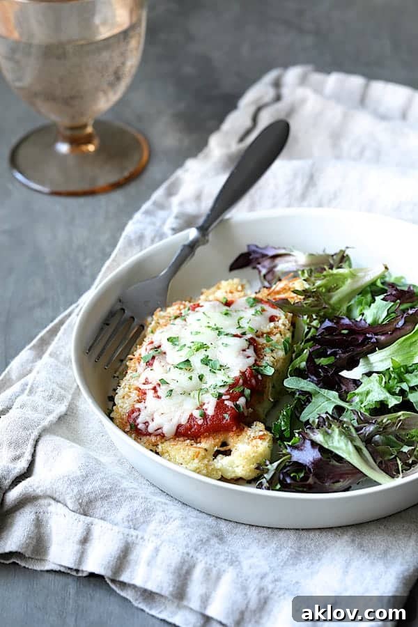 Close-up photo of Cauliflower Parmigiana in white dish with fresh baby greens.