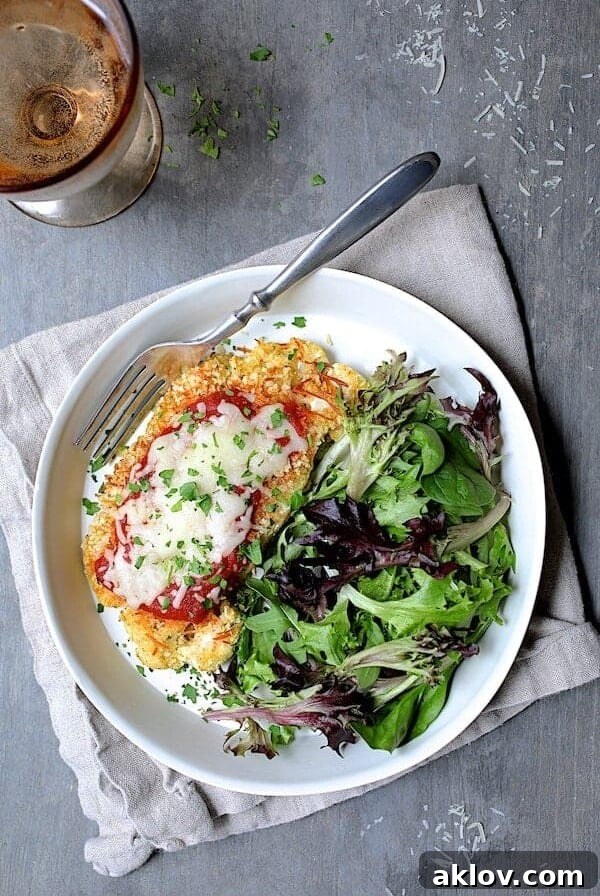 Cauliflower Parmigiana with salad greens on white plate on beige napkin.