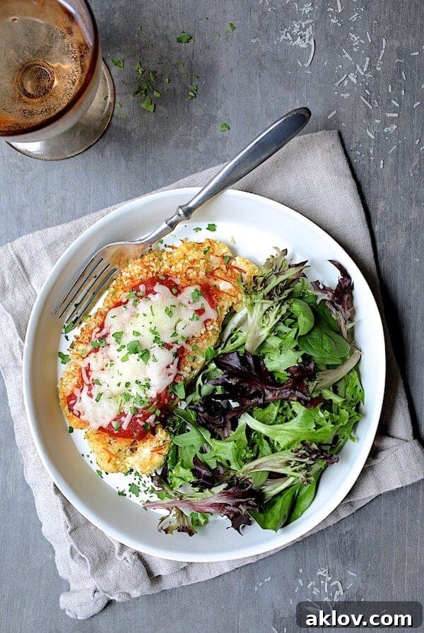 Cauliflower Parmigiana with salad greens on white plate on beige napkin.