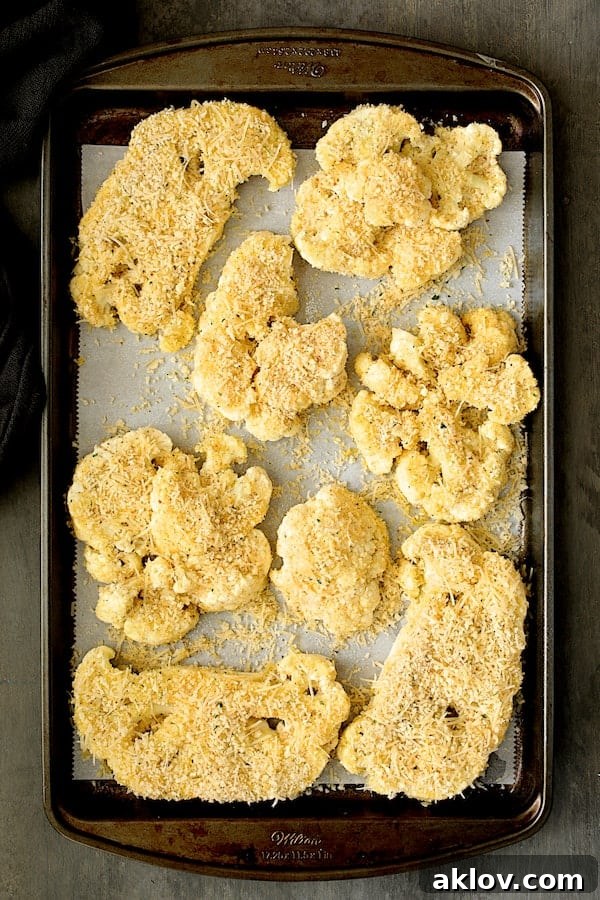 Cauliflower steaks meticulously coated with a savory mixture of breadcrumbs and Parmesan cheese, arranged on a baking sheet, primed for baking.
