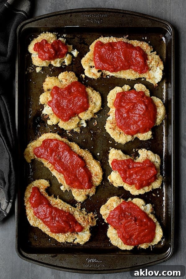 Baked cauliflower steaks generously covered with a rich and flavorful marinara sauce, poised for the final cheese topping.