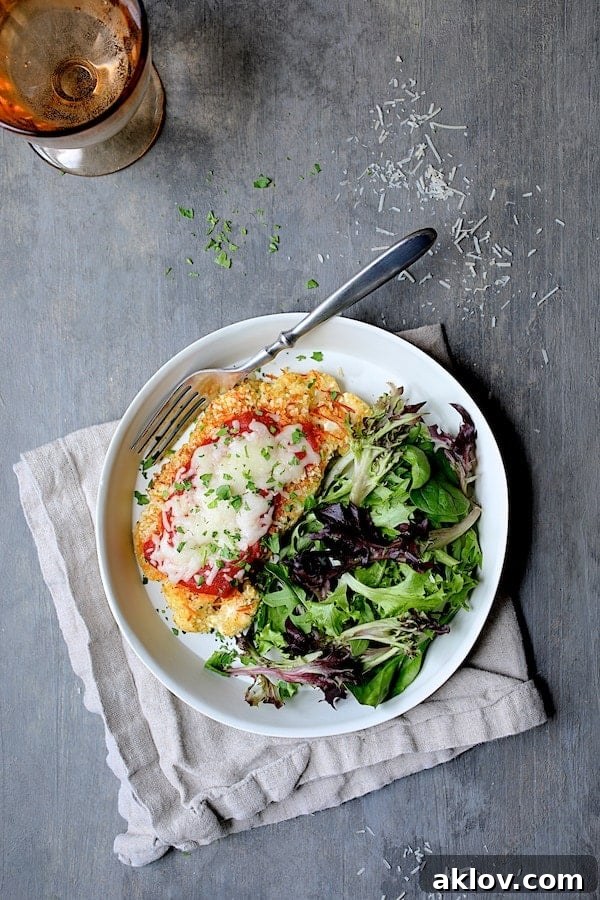 Photo of Cauliflower Parmigiana in white dish on beige napkin on gray background.