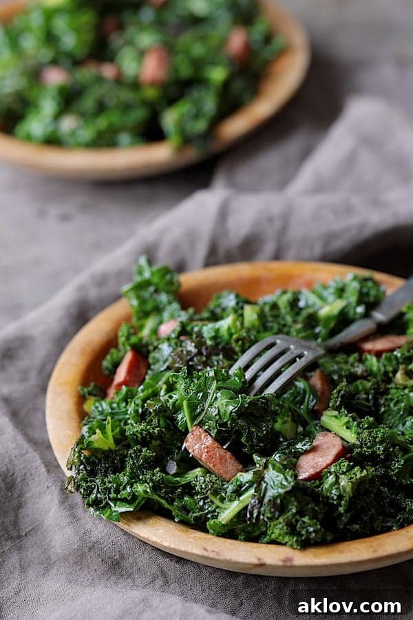 Spicy Sautéed Kale with Andouille Sausage - Straight-on close-up shot of dish on wooden plate with fork stuck into sausage and kale on gray background