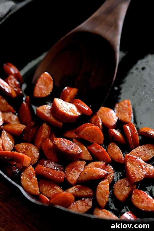 Photo of Andouille sausage being sauteed in cast iron skillet being stirred with wooden spoon