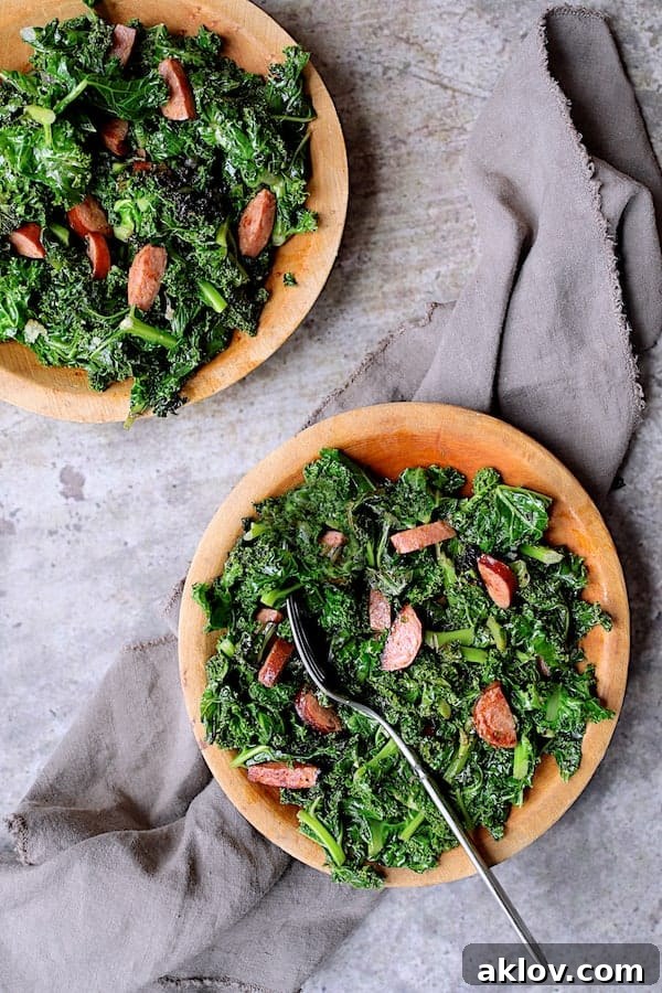 Spicy Sautéed Kale with Andouille Sausage - Overhead shot of dish on two wooden plates on gray background with gray napkin
