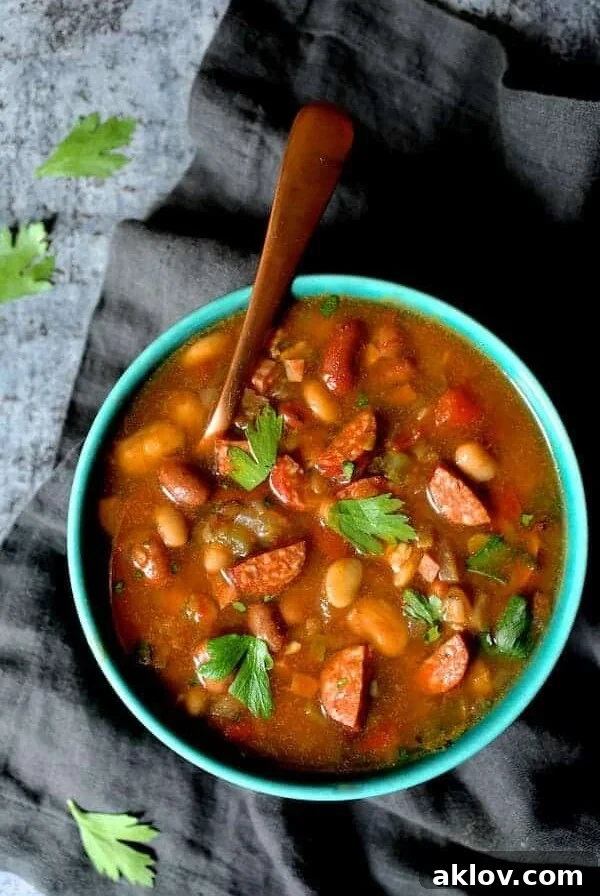 Slow Cooker Cajun 15 Bean Soup with Andouille Ham and Bacon in bright blue bowl with copper soup spoon.