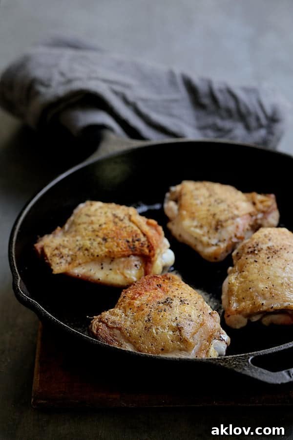Photo of browned chicken thighs in a cast-iron skillet, showing golden, crispy skin.