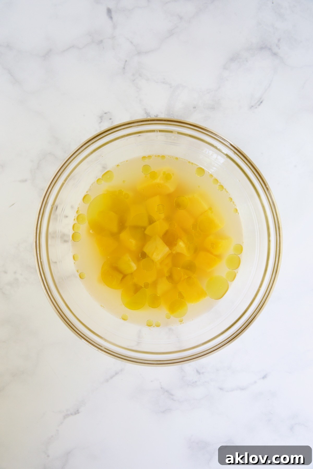 Mango chunks in water, rice vinegar, lime juice and olive oil in glass bowl.