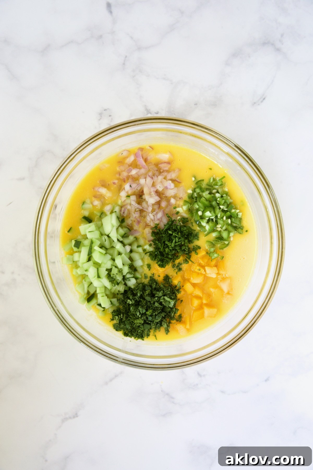 Cucumber, red onion, serranos, fresh mango, chives and cilantro in mango puree in glass bowl.