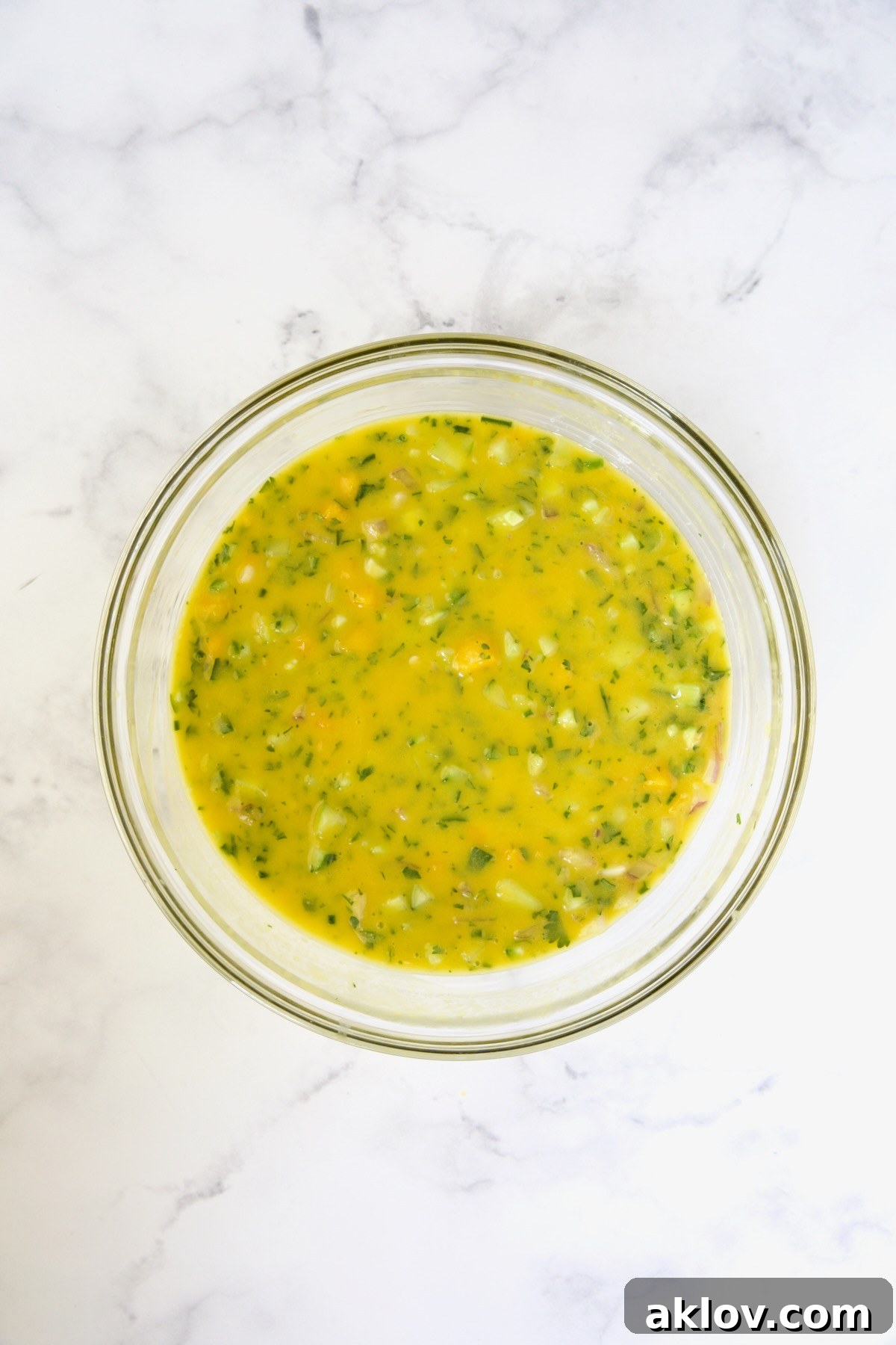 A luscious glass bowl of Mango Gazpacho, showcasing its creamy texture and vibrant color, with visible chunks of fresh ingredients stirred in, perfectly chilled and ready to serve.