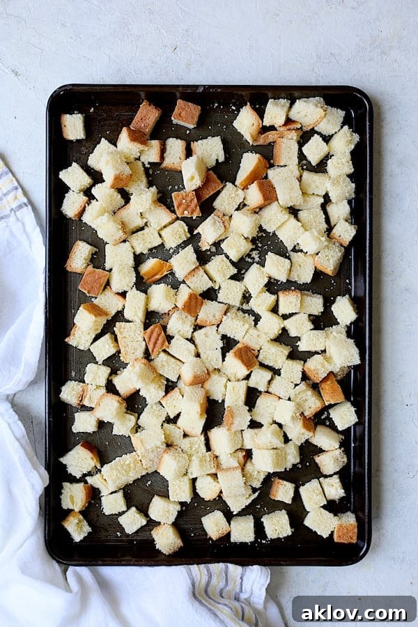 Cubed brioche bread spread out on a baking sheet, ready for toasting.