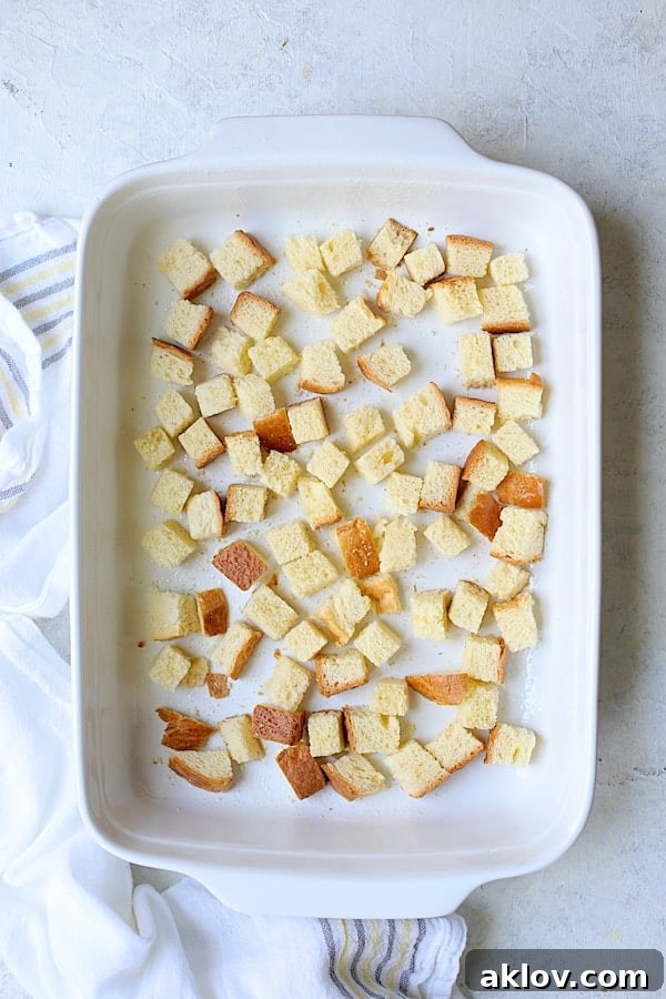 First layer of toasted brioche cubes neatly arranged in a white baking dish for the strata.