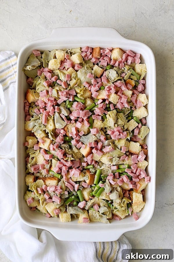 All layers of brioche, asparagus, artichokes, and ham completely assembled in the white baking dish, ready for the final touches.