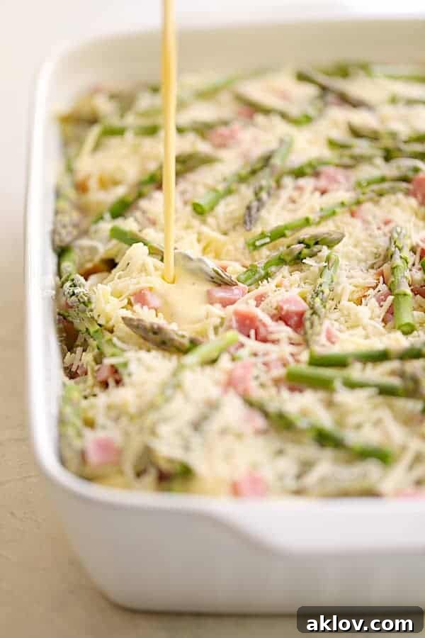 Rich egg and milk custard being generously poured over the layered breakfast strata in the white baking dish.