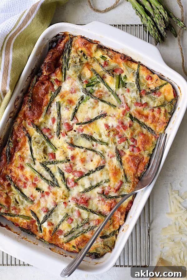 The freshly baked Breakfast Strata with Asparagus, Artichokes, Ham and Gruyere, golden and puffed, cooling in its white baking dish.
