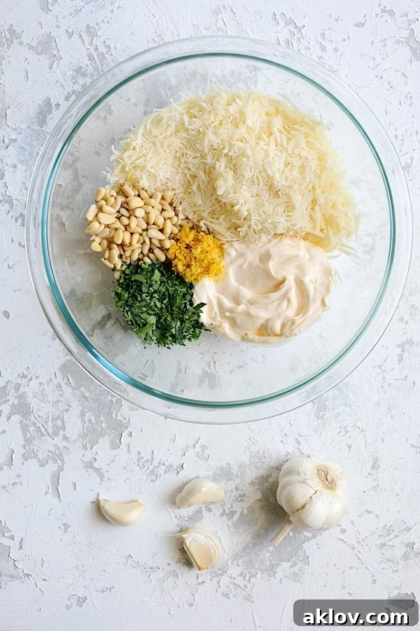 A glass bowl filled with the creamy, golden lemon parmesan stuffing mixture, showing flecks of green parsley and pine nuts.