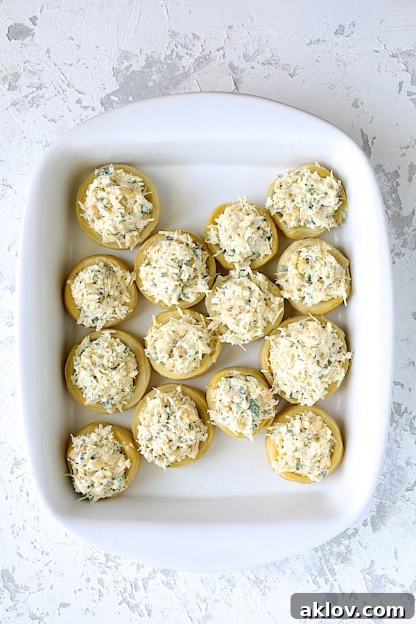 A white baking dish filled with artichoke bottoms, each generously stuffed with the lemon parmesan mixture, ready for the oven.
