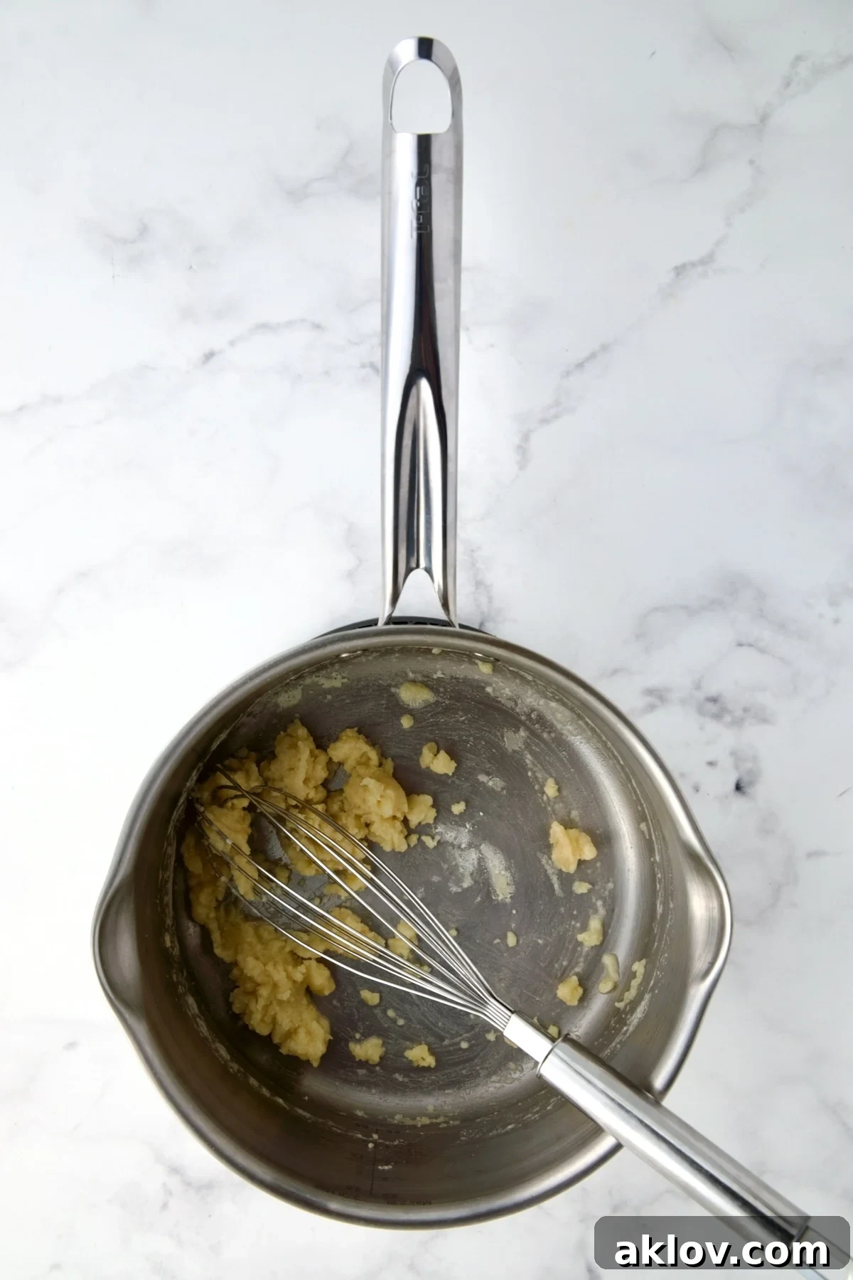 Roux, consisting of butter and flour, being whisked in a stainless steel saucepan, forming a creamy base.