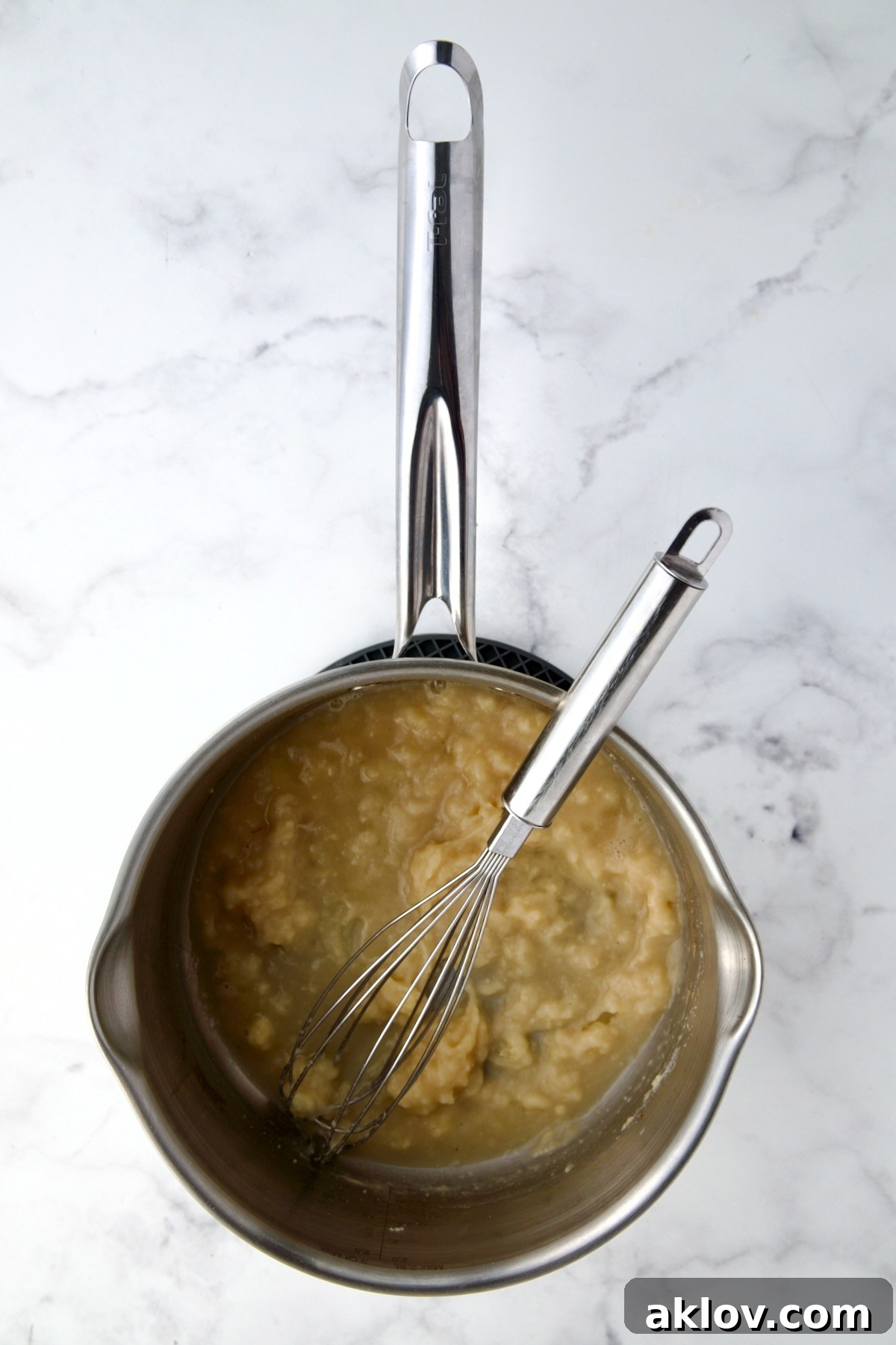 Butter, flour, and sherry being skillfully whisked together in a stainless steel saucepan, forming a rich paste.