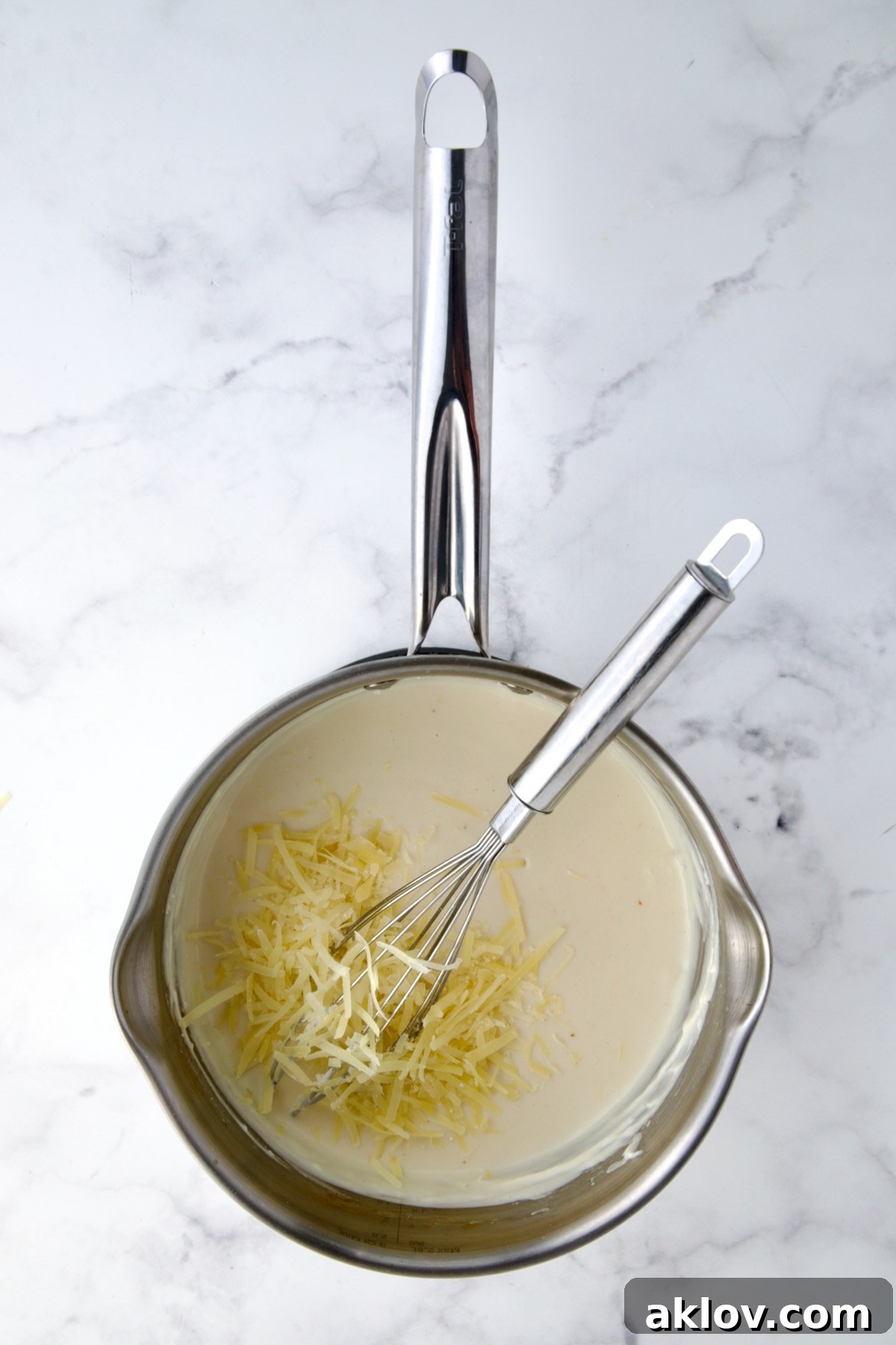 Grated cheese being gradually added to a creamy white sauce in a stainless steel saucepan, melting into a smooth consistency.