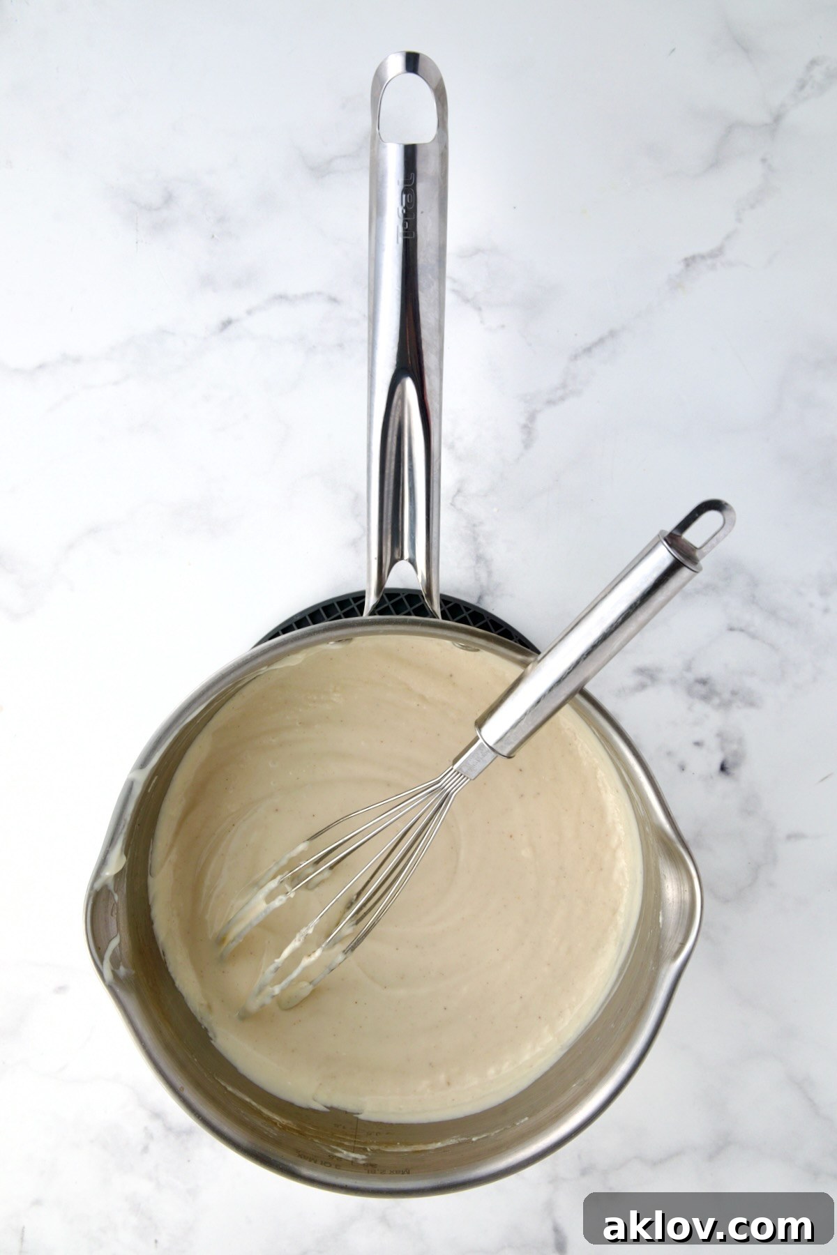 A perfectly thickened and smooth cheese sauce, with a wire whisk resting in a stainless steel saucepan, ready for assembly.