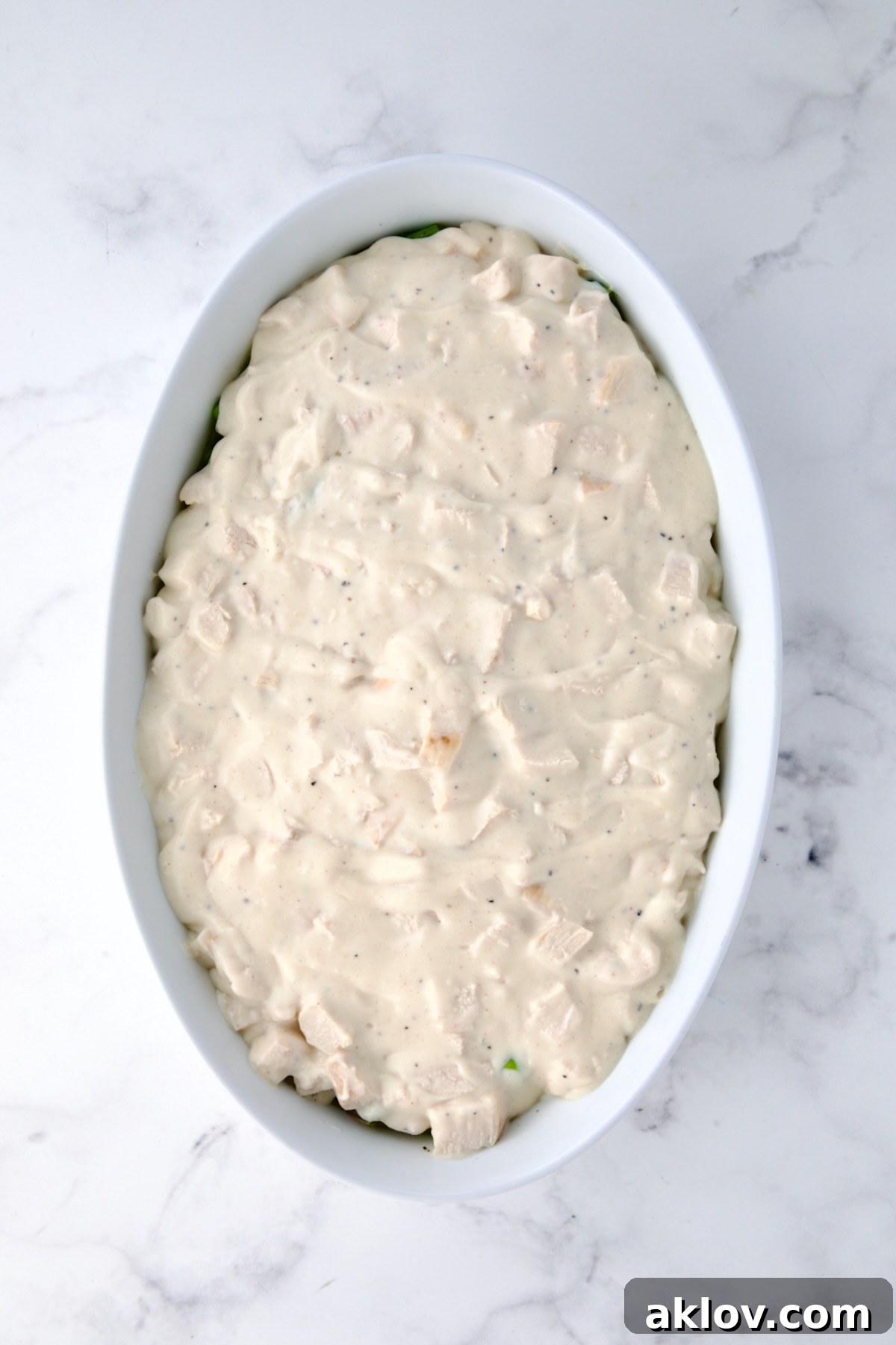 Delicious cheese sauce with diced chicken generously poured over a bed of blanched asparagus in an oval baking dish, ready for baking.