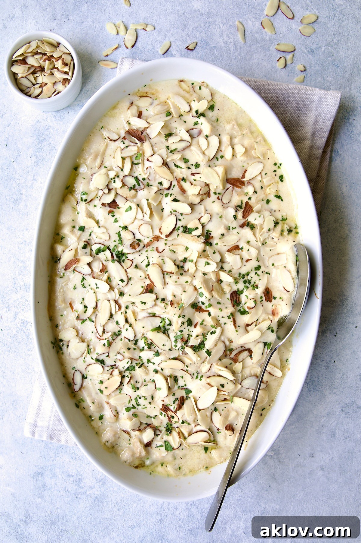 Golden-brown Chicken Divan with Asparagus, garnished with toasted sliced almonds, presented in an oval baking dish with a serving spoon.