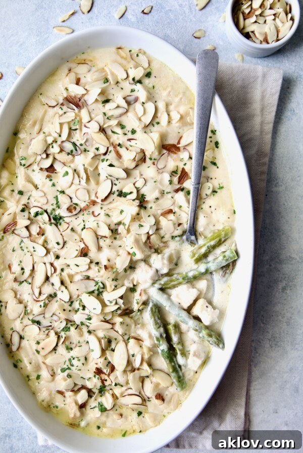 Chicken Divan with Asparagus in oval baking dish with serving spoon garnished with sliced almonds with asparagus and chicken exposed.