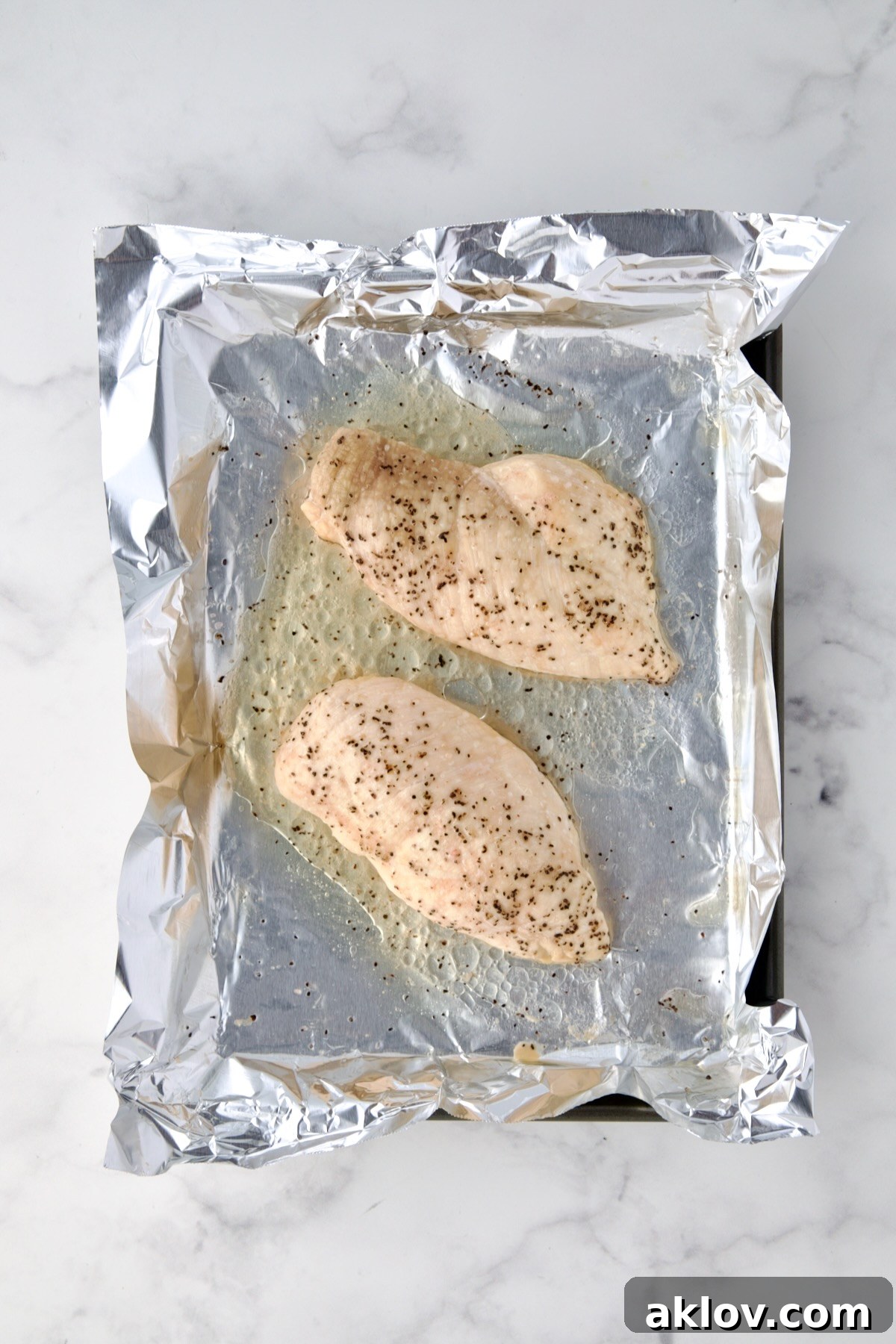 Two perfectly roasted chicken breasts resting on an aluminum foil-lined baking sheet after baking.