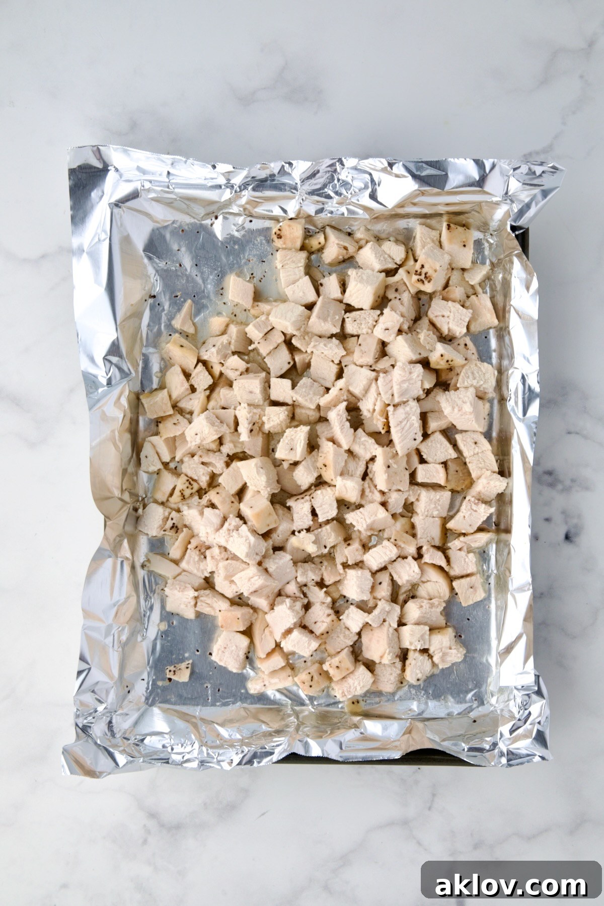 Cubed roasted chicken pieces, evenly cut, arranged on an aluminum foil-lined baking sheet.