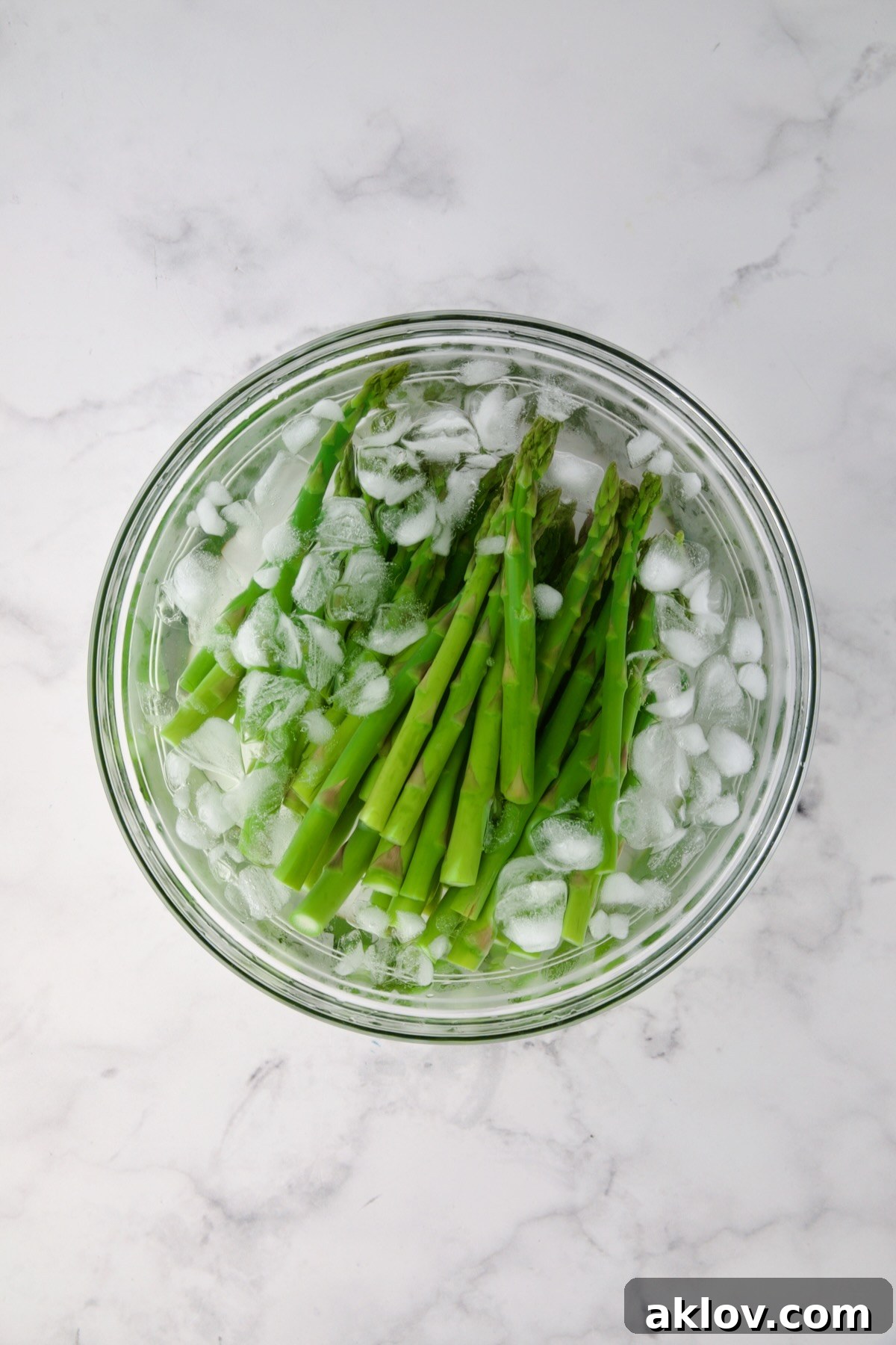 Vibrant green blanched asparagus cooling in a refreshing ice bath to preserve its crispness.