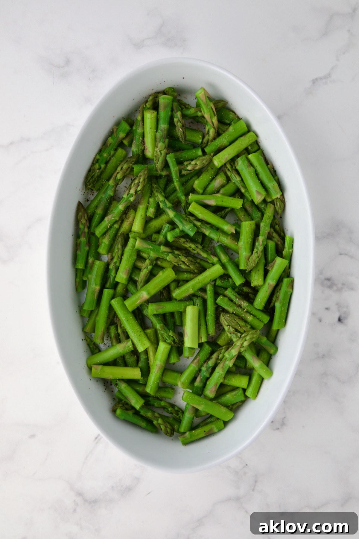 Blanched asparagus, neatly cut into pieces, arranged at the bottom of an oval baking dish, ready for assembly.