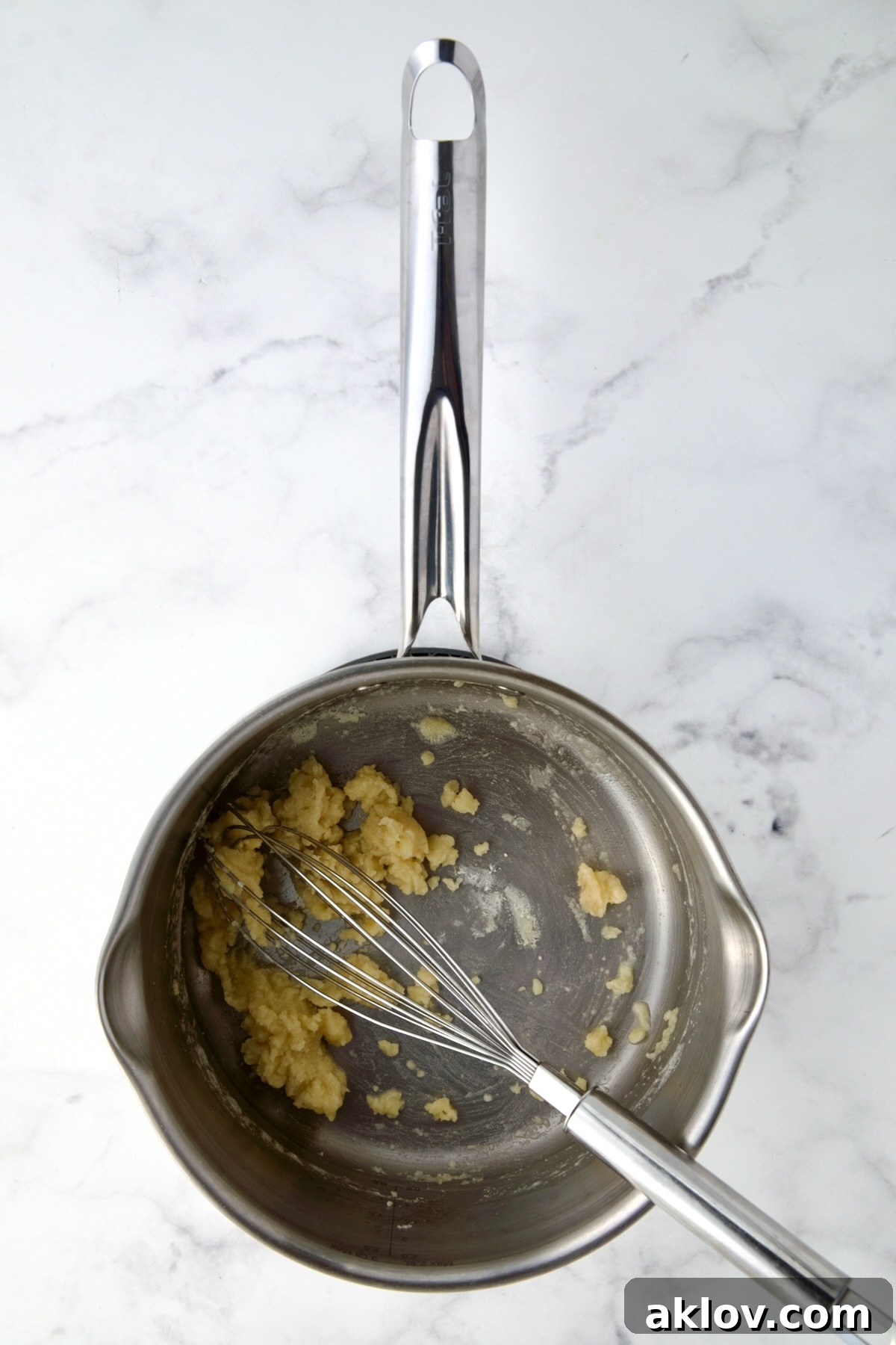 Butter and flour being meticulously whisked together in a stainless steel saucepan to create a smooth roux.