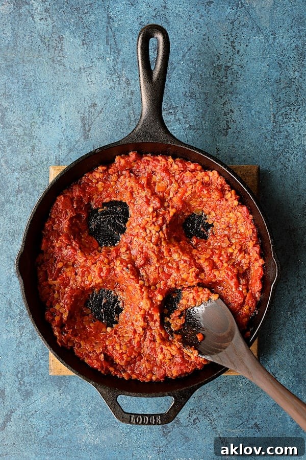 Four perfectly formed wells created in the rich tomato and lentil mixture within a cast iron skillet, ready to receive the eggs for poaching.