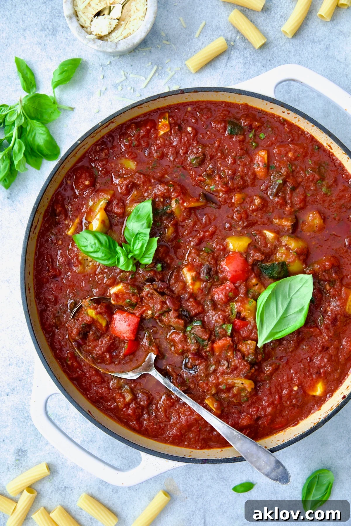 Veggie Pasta Sauce in white enamel cast iron skillet with serving spoon garnished with fresh basil.