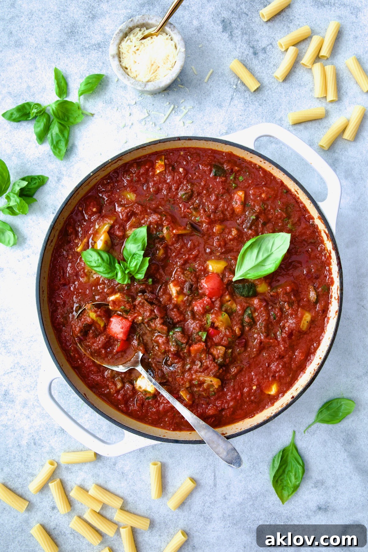 Veggie Pasta Sauce in white enamel cast iron skillet with serving spoon garnished with fresh basil.