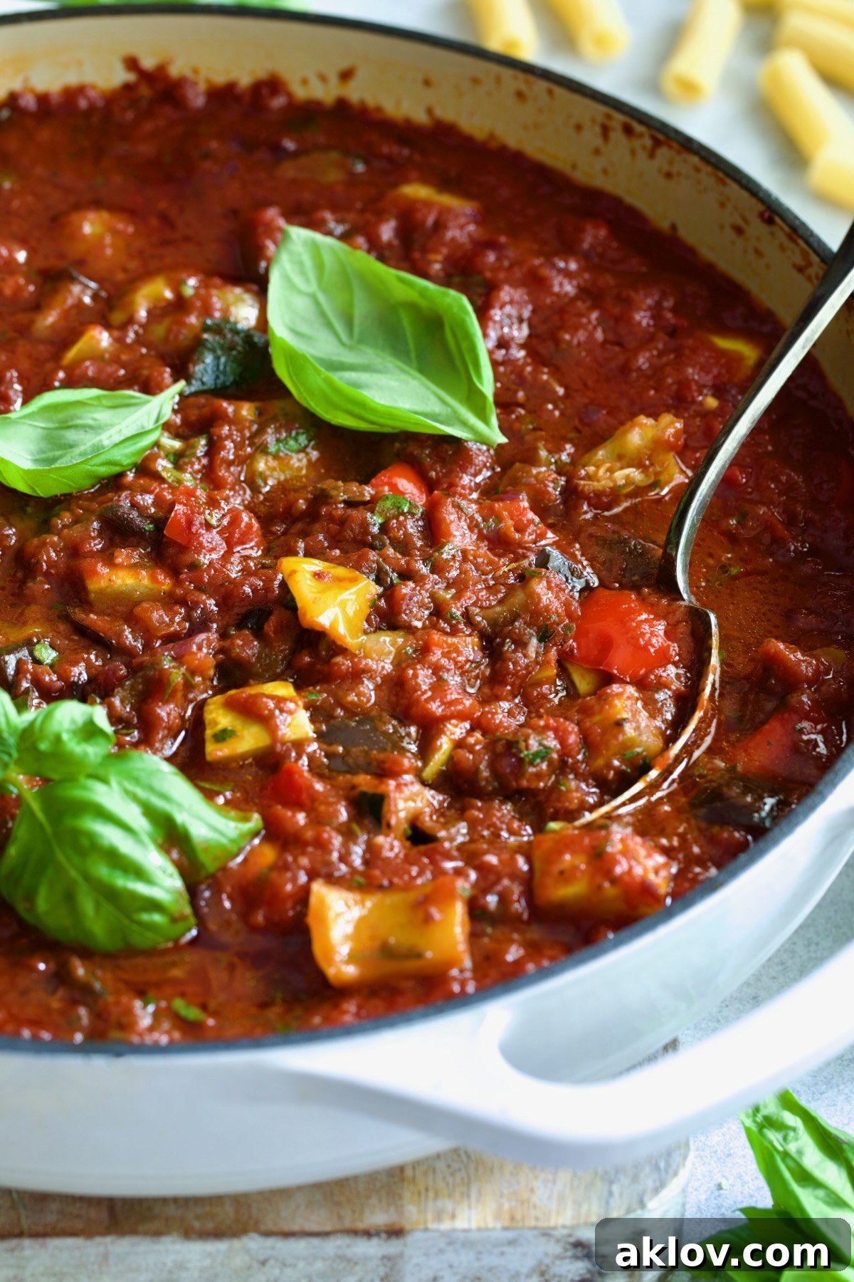 Veggie Pasta Sauce in white enamel cast iron skillet with serving spoon garnished with fresh basil.