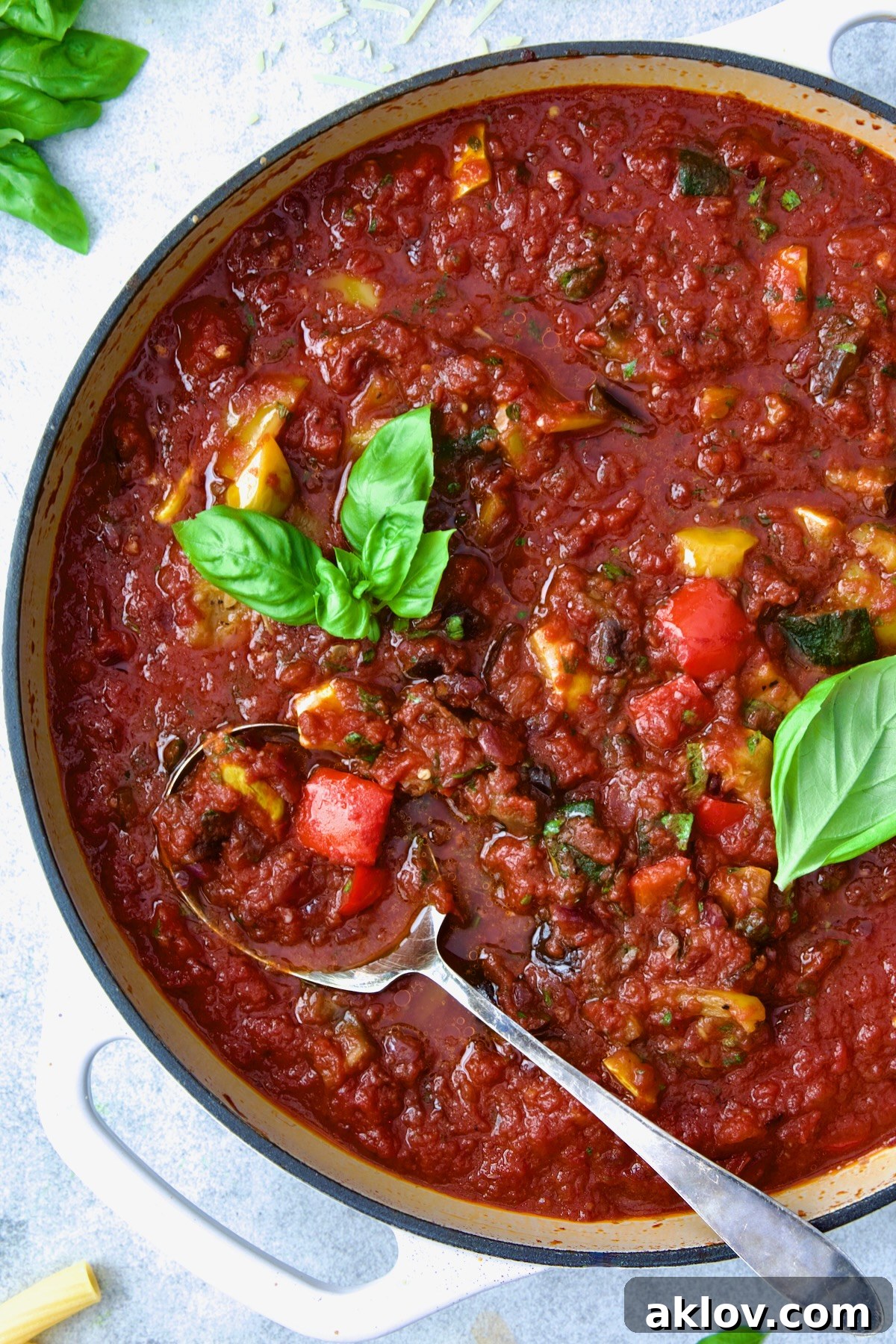 Veggie Pasta Sauce in white enamel cast iron skillet with serving spoon garnished with fresh basil.