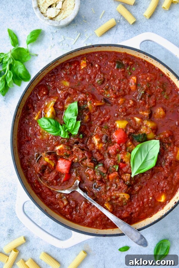 Veggie Pasta Sauce in white enamel cast iron skillet with serving spoon garnished with fresh basil.