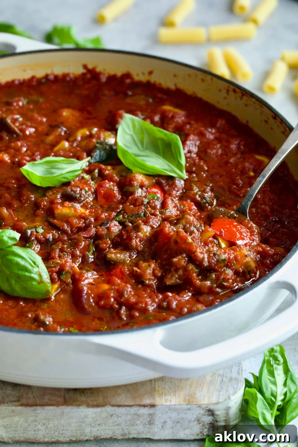 Veggie Pasta Sauce in white enamel cast iron skillet with serving spoon garnished with fresh basil.